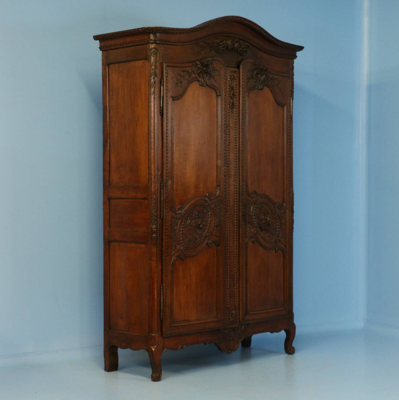 Richly carved french armoire with intricately carved florals, basket, and muscial instruments that was likely a wedding cabinet. The aged crack on the right door and other minor cracks are indicative of its age, adding to the character and beauty of
