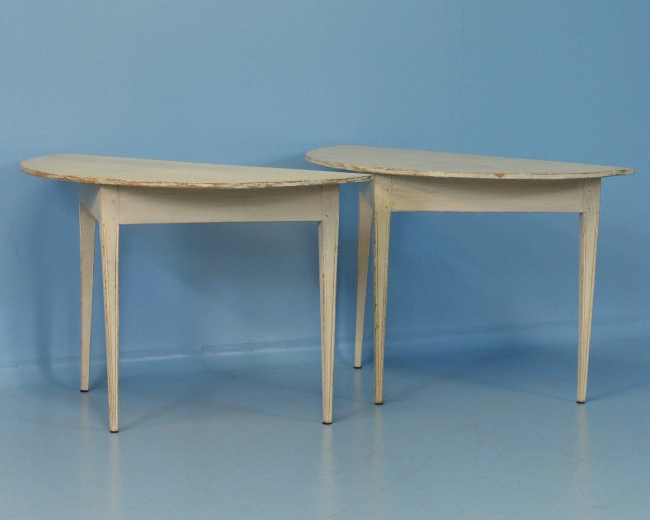 Lovely lines grace the silhouette of this charming pair of Swedish Demi-Lune pine tables. Note the gently tapered legs with simple carved dentil detail and the wood pegs used instead of nails. The original white paint has been distressed, revealing