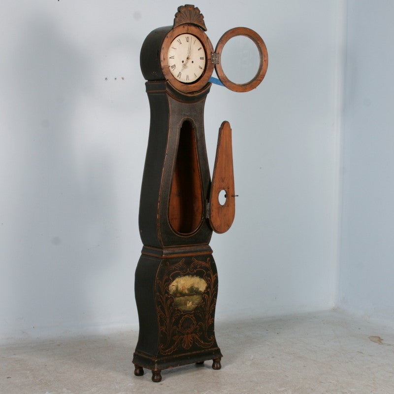 Swedish Mora Grandfather Clock. This lovely grandfather clock boasts the traditional curves of the Swedish Mora design. The original black paint is accented with gold flourish detail, while the bottom has a lovely pastoral scene with lake and swan