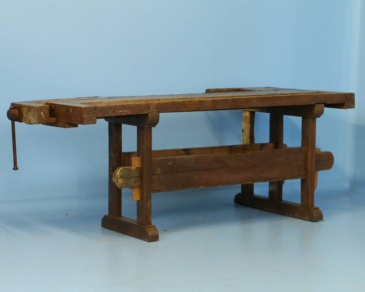 The warm patina on this workbench comes from the years of constant use, while the base still maintains an aged painted finish. It has two vices and a recessed tray where the carpenter would lay his tools. Note the lower shelf that rests between the