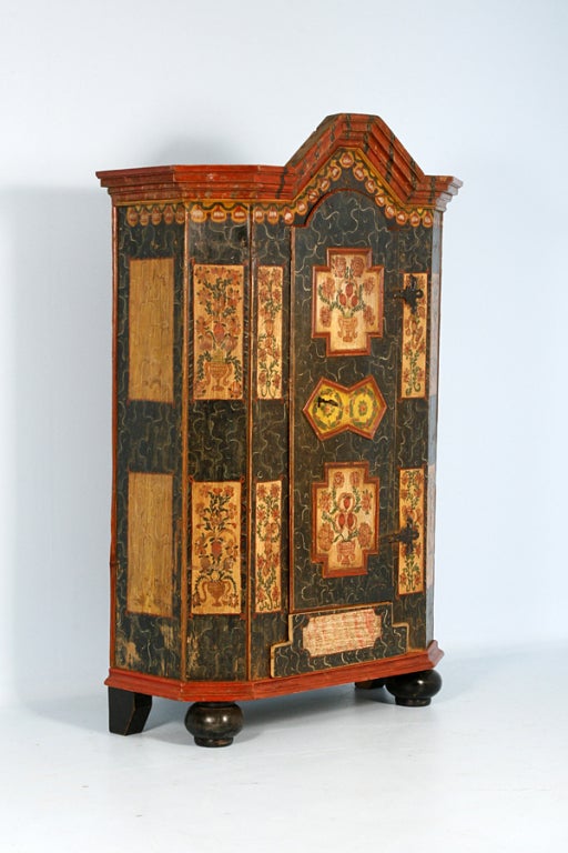 This stunning hand-painted armoire has rich, deep autumn colors of orange, green, ochre, and a very dark blue verging toward black. Intricate floral motifs surrounded by artistic flourishes encompass the entire front and sides of the piece. This