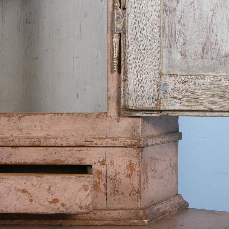 The lovely distressed paint on this corner cupboard is all original. The exterior is a pale pink and the interior  white. The gentle carving of the gothic gallery top add to its country appeal. Please note the close up photo of the base reveals that
