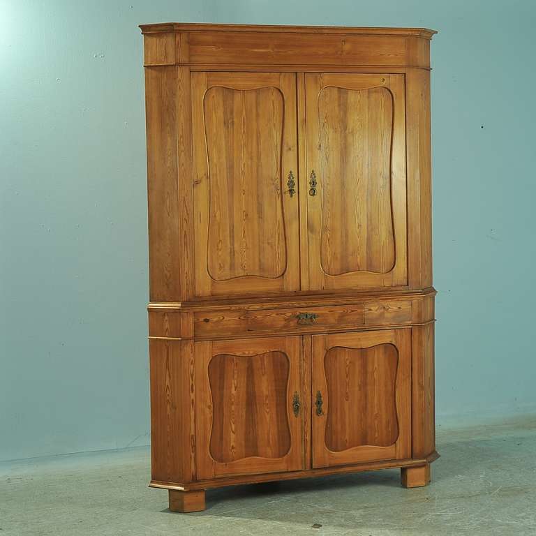 Large scale corner cabinet from Sweden. The age of the piece is reflected in the darker patina of the pine, which has been given a wax finish. Interior shelving and central drawer provide ample storage options. Depth from back corner to front/center