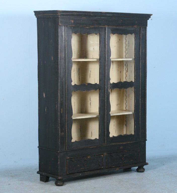 This Original Antique Danish pine cabinet has been restored with a new hand painted distressed black finish on the outside and eggshell finish on the inside. The lovely scalloped edging around the glass doors and lower two drawers adds to the simple