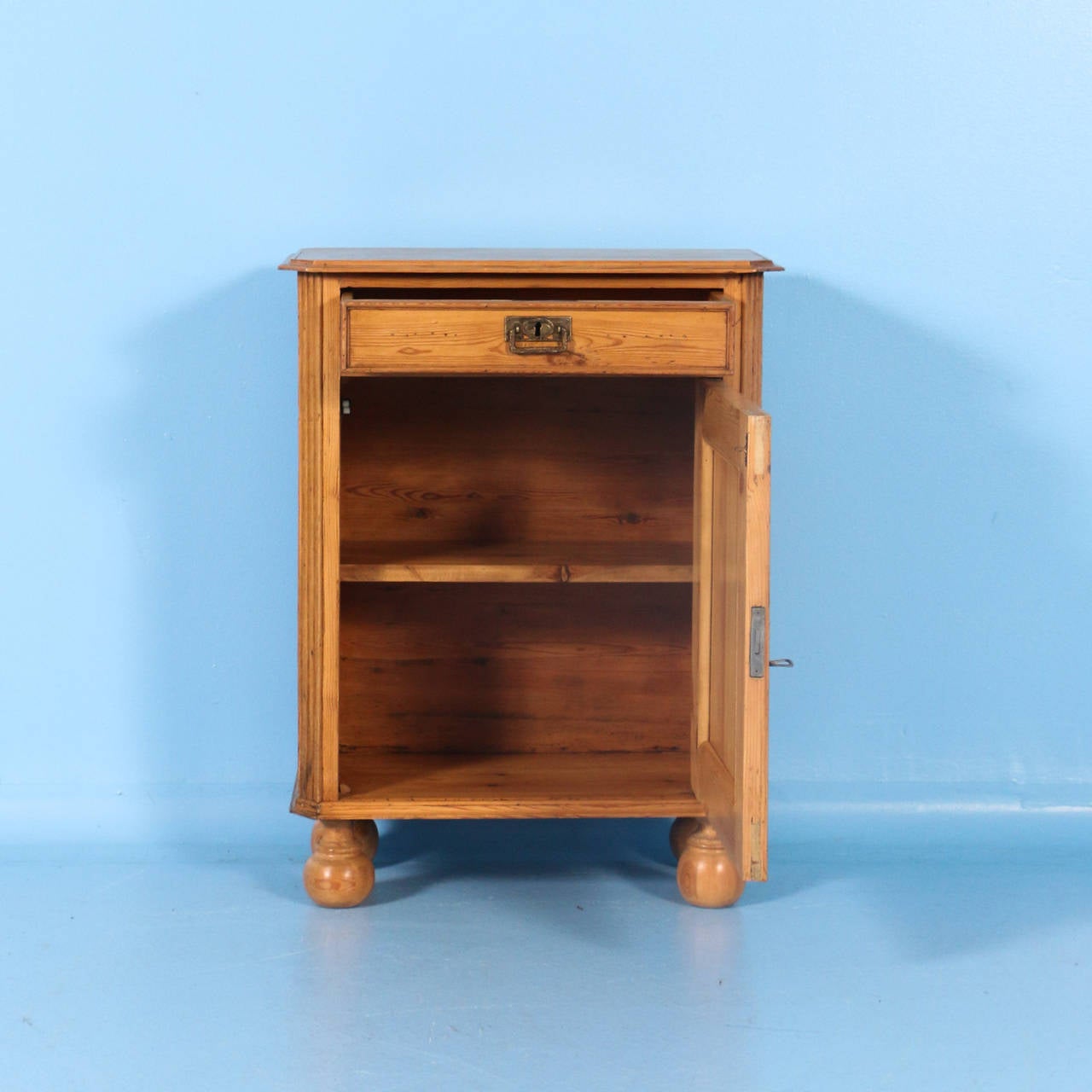 This Danish Pine nightstand has the traditional one drawer over one door for storage. It  has been given a wax finish, bringing out the warmth of the pine. Simple carved dentil molding along the sides add to its charm. The current feet are original