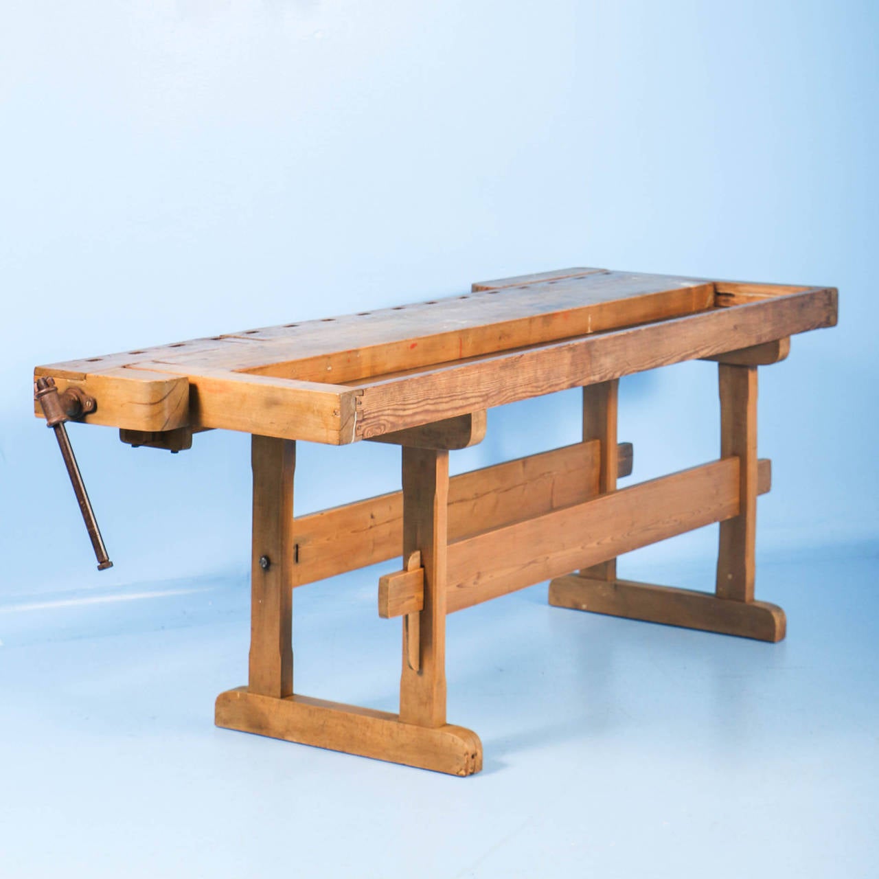 The light pine patina on this workbench comes from the years of constant use. It has two vices(one with iron handle, one of wood) and a recessed tray where the carpenter would lay his tools. The traditional trestle base allowed it to be assembled