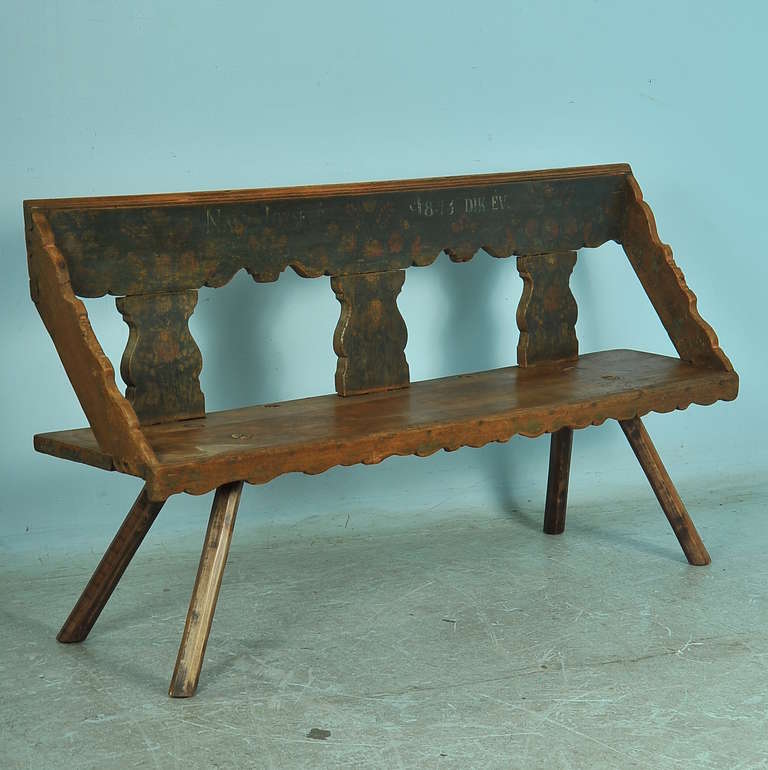 The original paint on this  European country style bench has been worn down to a perfect patina over many years of use. The seat and arms, which received the most wear, reveal the aged pine while the back still maintains the floral pattern,