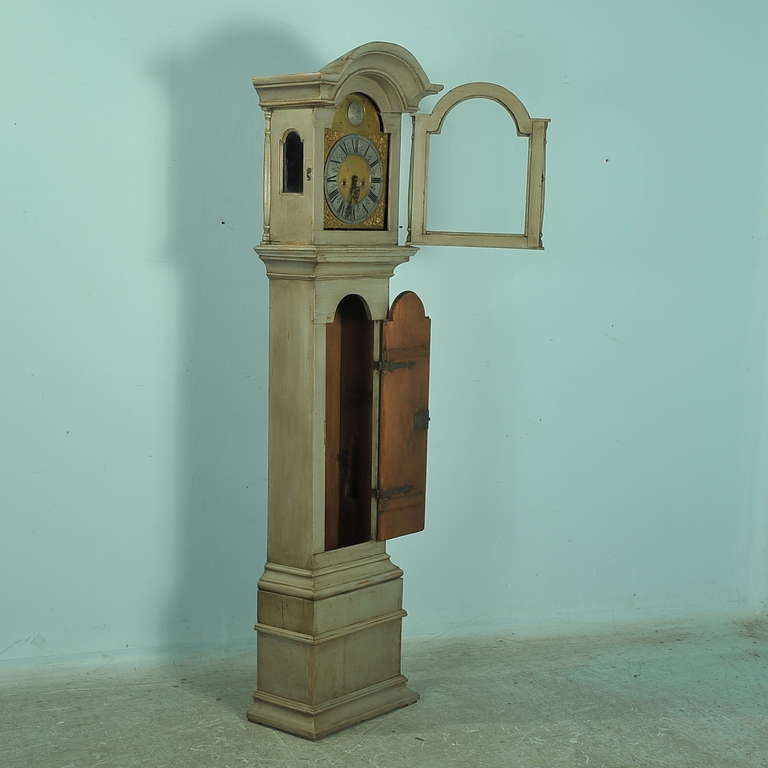 The sophisticated style of this grandfather clock is due to the clean lines, elaborate face, and enticing painted finish. The grey paint is new, but has been gently distressed and blended to fit with the age and character of the clock, adding to the