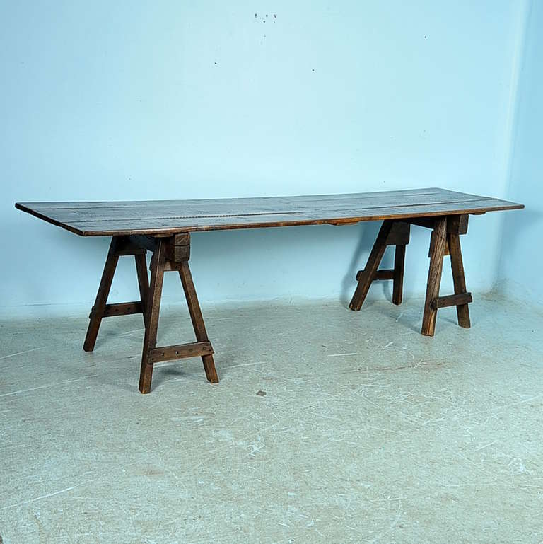 The rich vintage look of this table is enticing, and draws one in to touch the aged, worn top. The deep patina is the result of years of use, adding tremendous character to this table. Note the close up photos of the rustic wood saw horse bases, and