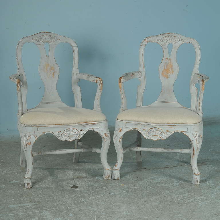 Gentle curves and carving accentuate this charming pair of Swedish arm chairs. The soft, distressed white paint and curved arms and legs add a romantic feel to the pair. The linen seats are newly upholstered; these chairs are solid and ready to be