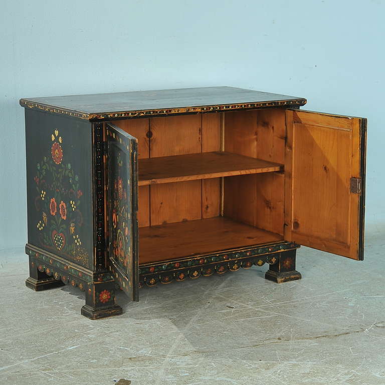 This highly decorative cabinet brings folk art charm life. It is a 2 door cabinet painted black, with traditional flowers, hearts, and leaf/vine motif embellishing the entire piece. Fun and whimsical, this original painted piece will add a vibrant