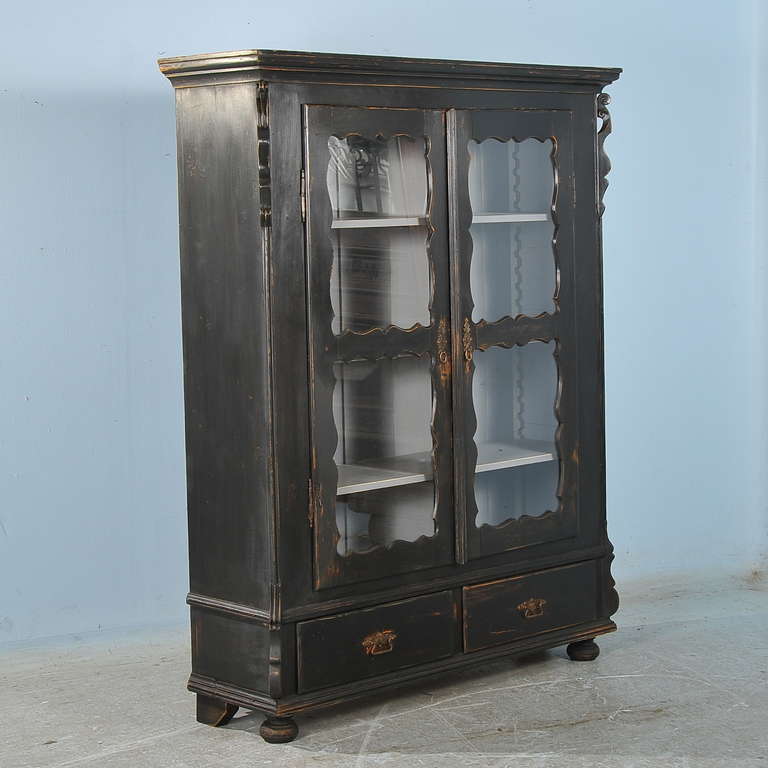 This lovely black cabinet or bookshelf has glass doors accentuated with curvaceous carved panels which both protect and highlight the books or collectibles stored within. The shelves are adjustable, allowing for easy storage and display of taller or