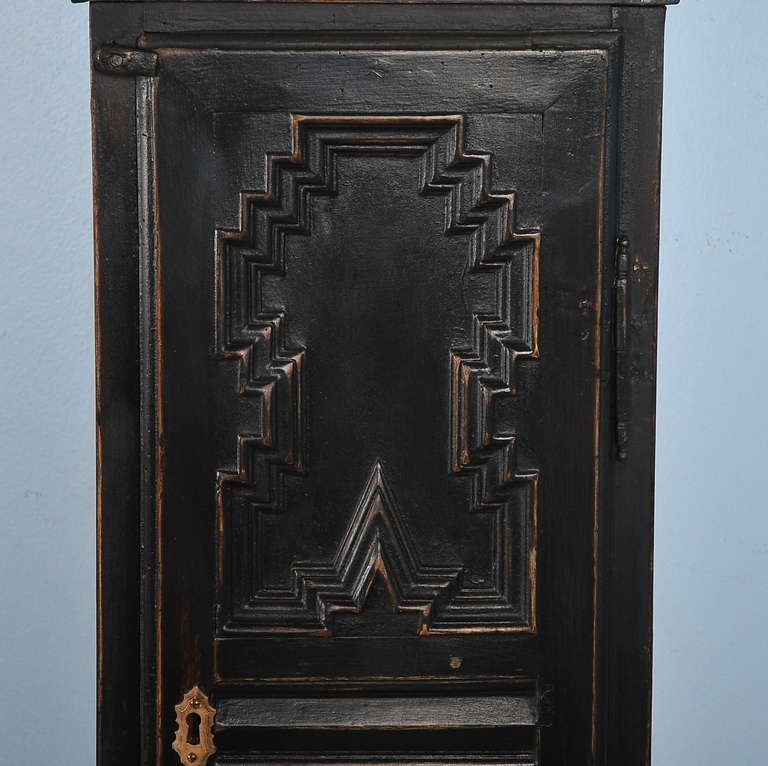 Intriguing geometric carved panels accentuates the strong lines of this black painted grandfather clock from Denmark. Note the ornate face with etched brass and filigree work. Above the face is a monogrammed centerpiece as well. When this clock was