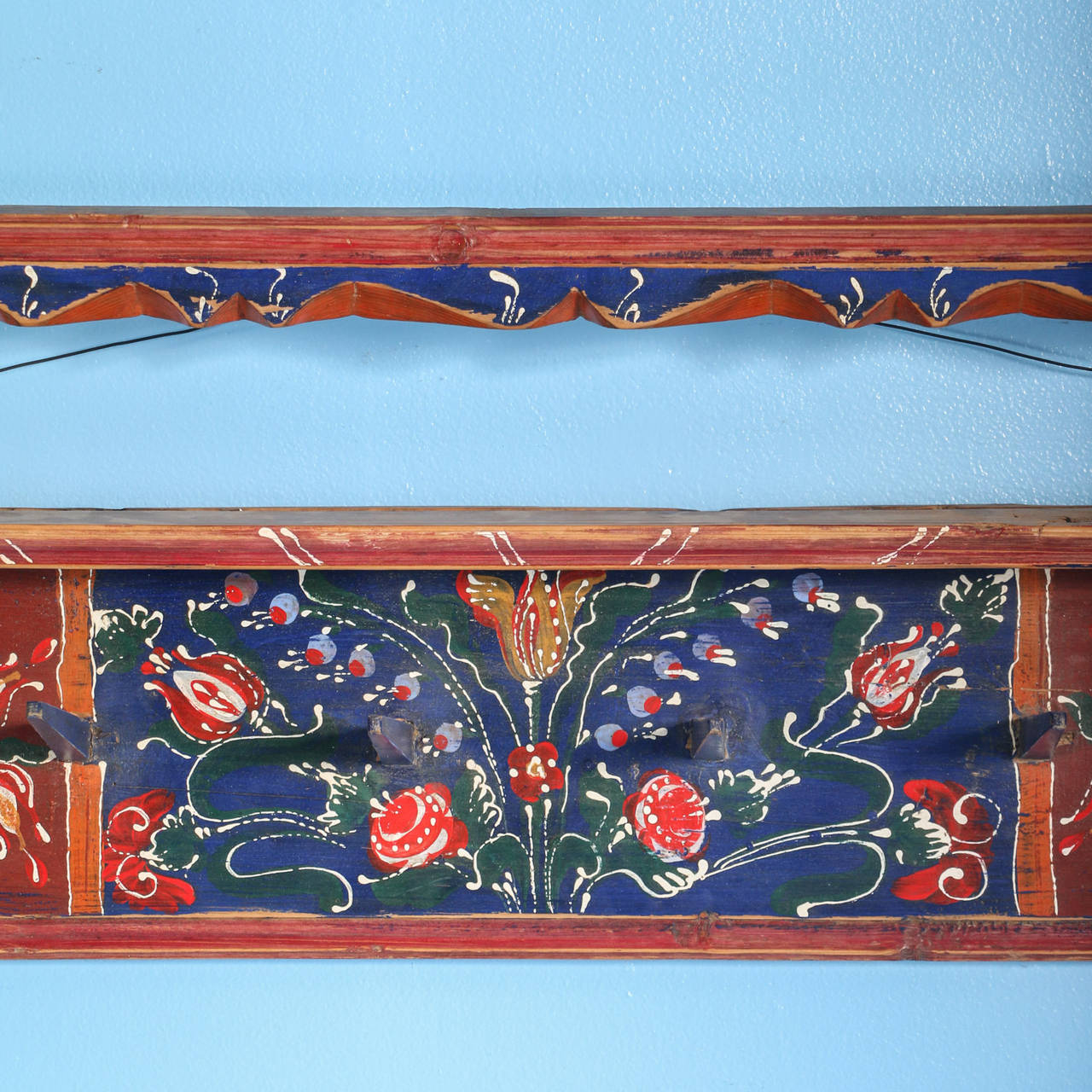 The striking blue, red, and green paint is all original on this painted rack from Romanian. It was painted in a traditional folk art style with flowers. This was originally a hanging plate rack; the plates would be displayed above while coffee mugs
