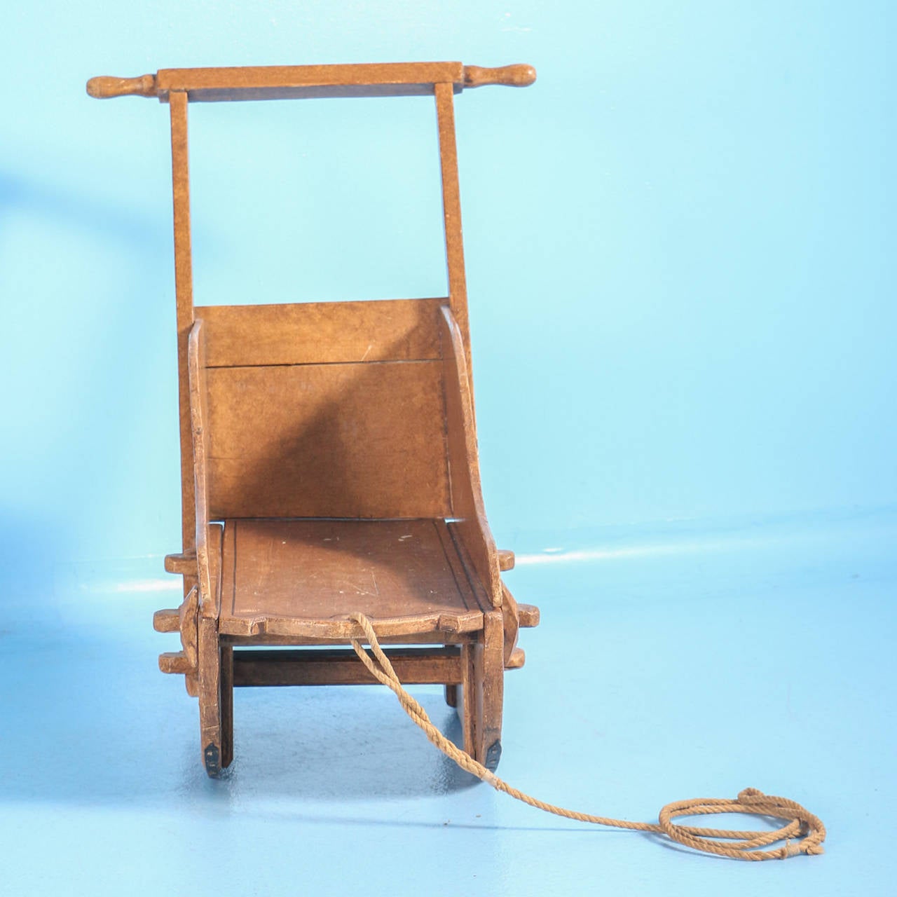 This delightful wooden sled was built for a child. Note the small scale and rope still attached to the front for pulling and tall handle in the back to push.