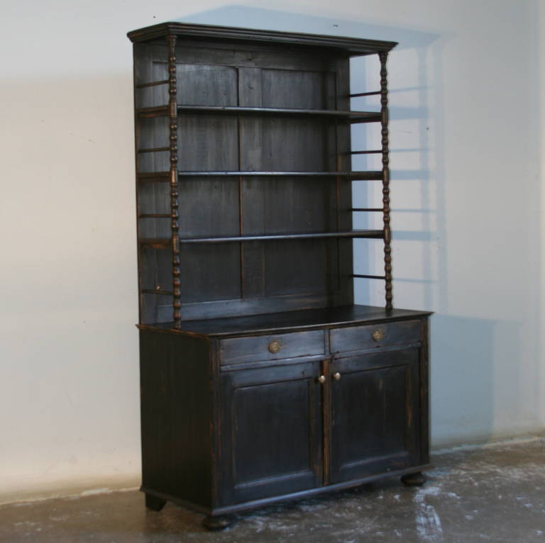 This lovely old pine cupboard has open shelving, allowing it to be used as a bookshelf or cabinet as well. The turned columns that support the shelves add a touch of intrigue to the look. While the piece is old, it has been given a new painted black