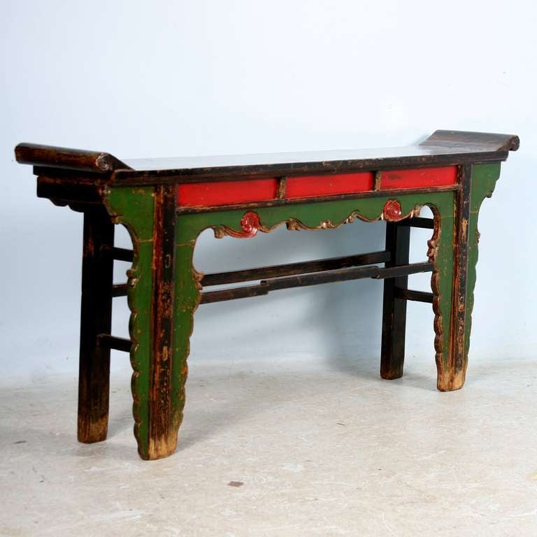 This console table is from the Shandong Province of China and boasts impressive, strong colors and hand carved details. Unique carving abounds in this piece, with the intriguing shape of the legs, two carved rosettes painted red, and the traditional