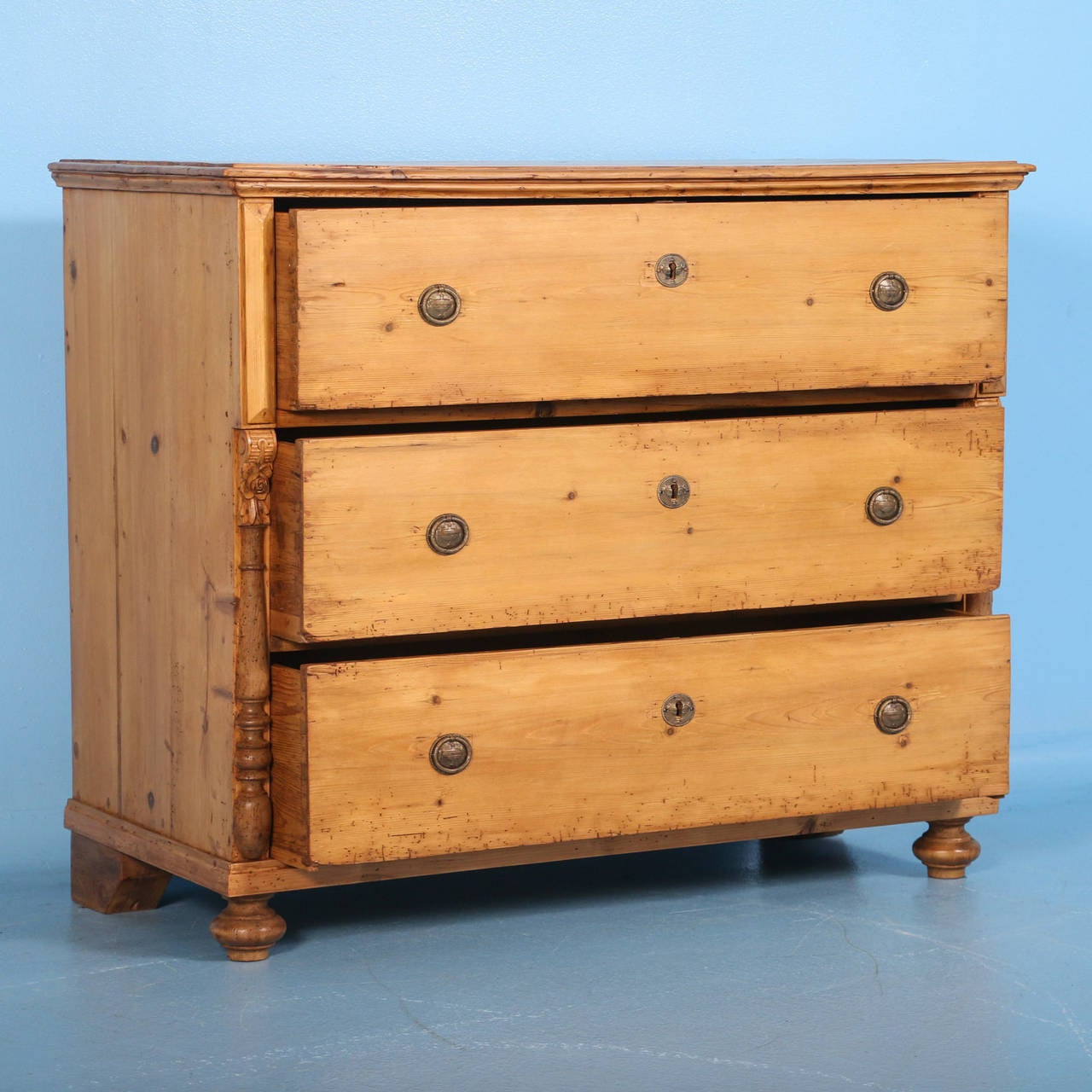 The top drawer slightly extends beyond the bottom drawers in this chest of three drawers. The half column details topped by a carved flower add to the charm of the piece. The pine has been waxed, bringing out the warmth of the wood and all the