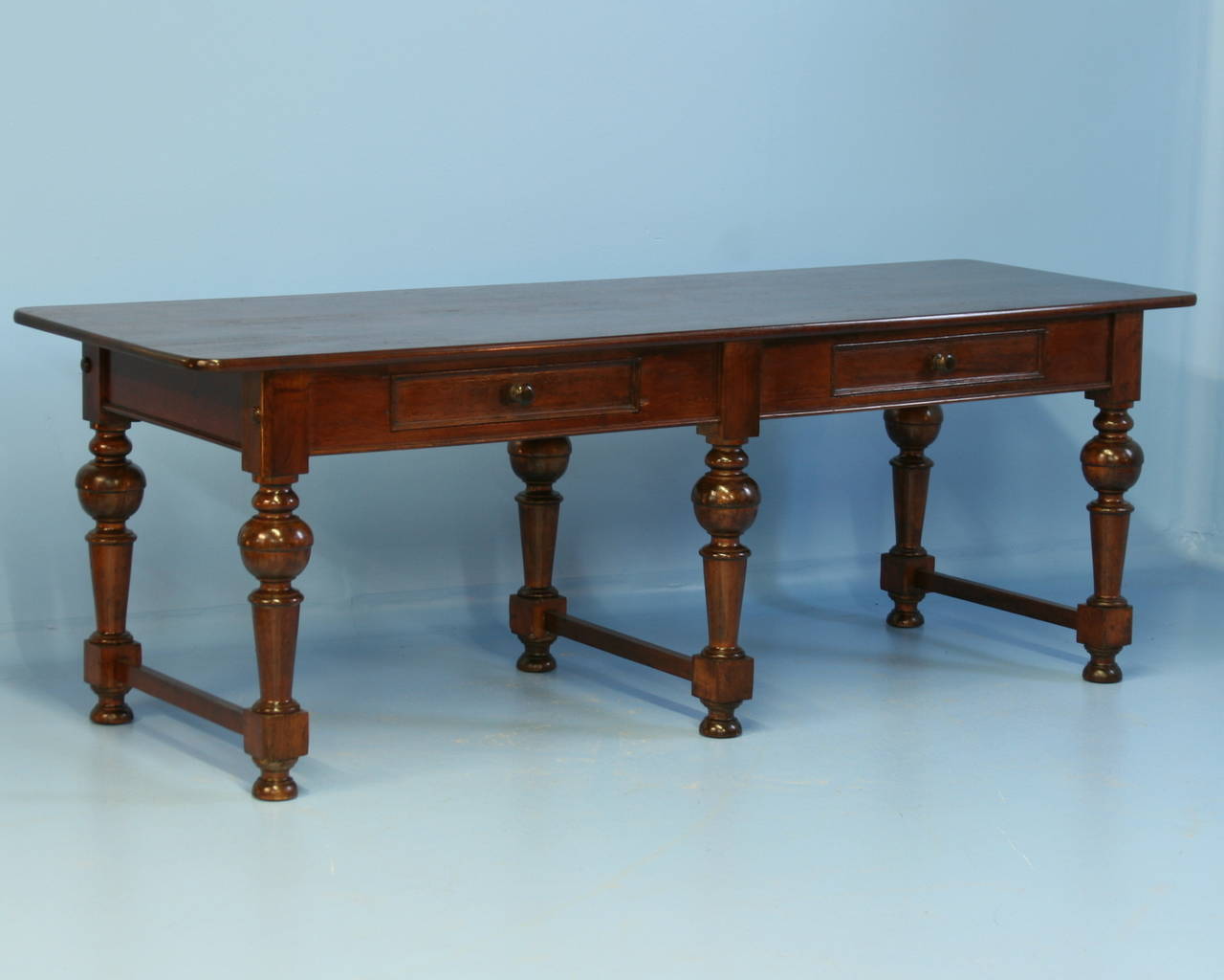 The amazing patina of this long table is due to the beauty of the rich mahogany top. The six turned legs with vertical stretchers add to the sophisticated look as well. With the 2 drawers, it likely served as a library table in its early life. This