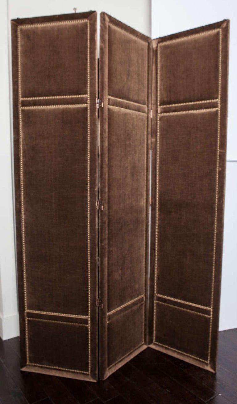 Three-panel folding screen is upholstered in brown striade velvet and is adorned with antique brass tacks.