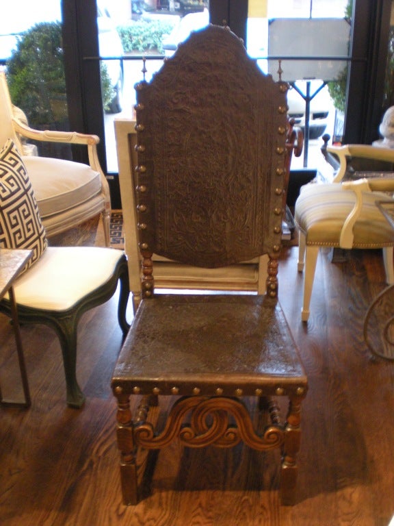 Carved walnut and embossed leather chairs. Four side chairs. Brass studs and finials. Distressed leather.