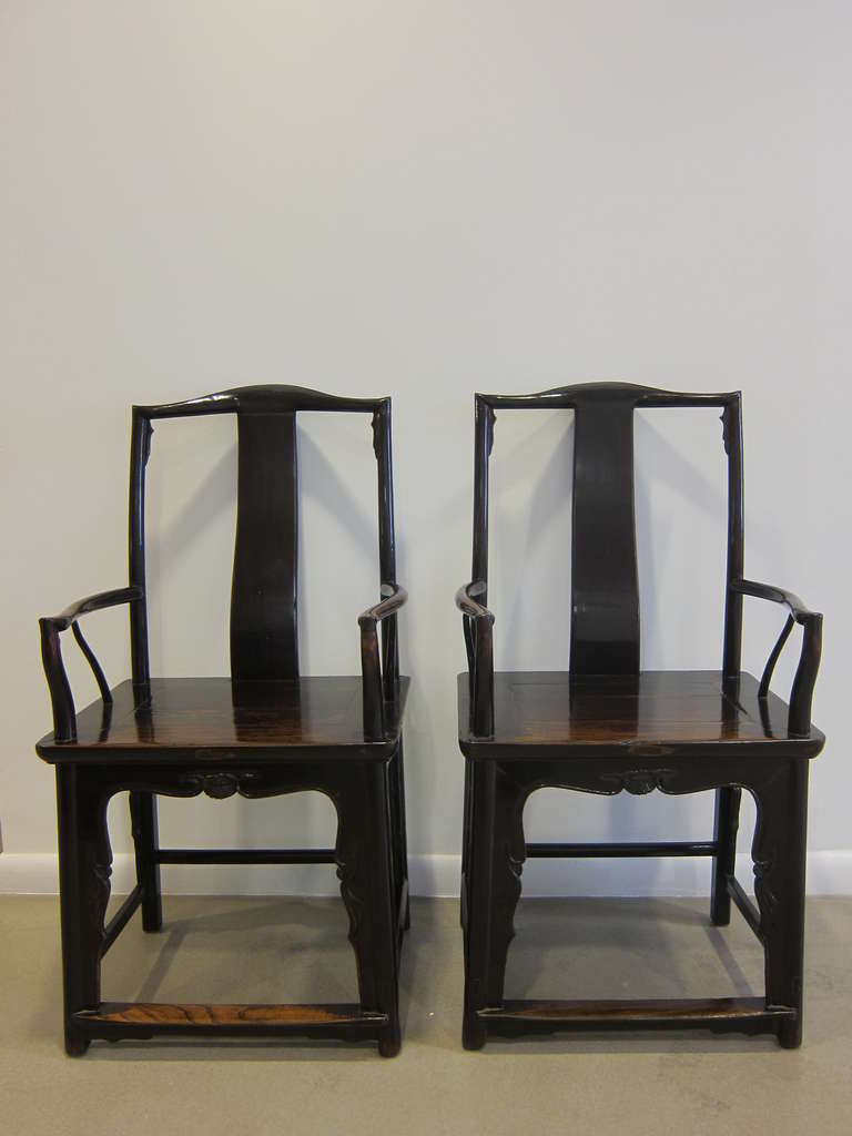A pair of 19th century Chinese Officials Hat Chairs.  Dramatic details include yoke back splat, carved spandrels to upper backrest corners and armrest joints also carved scalloped aprons below the seat. Elm wood with lacquer very good condition. 
