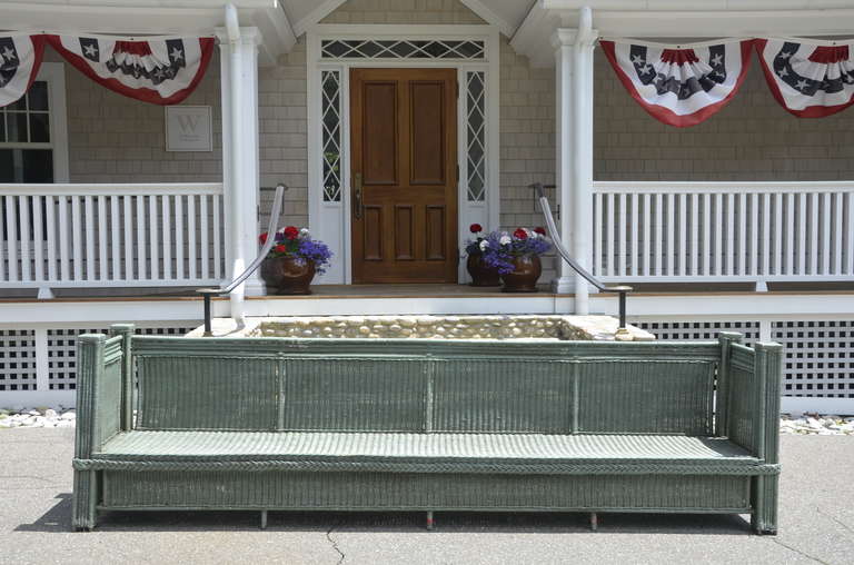 Custom built 11 foot wicker bench in green paint.  One of a kind in faded green paint with original vinyl cushion. Paint is chipped in some areas due to age.  A unique and rare piece.