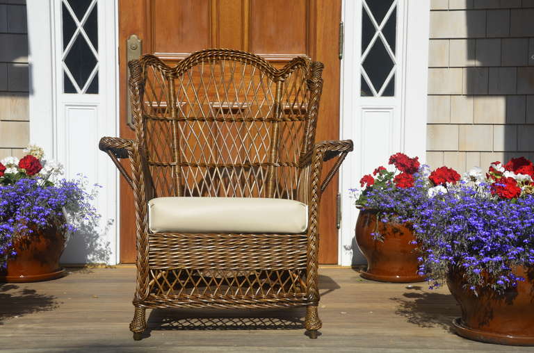 Beautiful antique wicker arm chair in natural finish.  Curved top and woven finials along with woven feet make this a unique piece.  Chair comes with a separate drop-in spring seat.