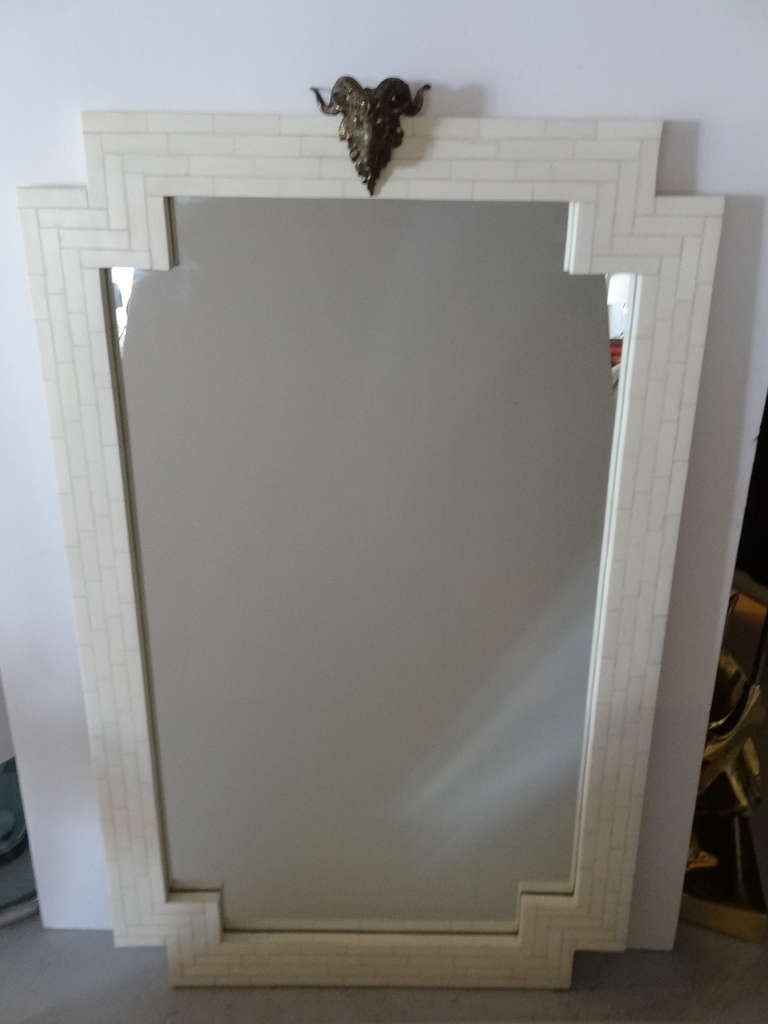 A large tessellated bone mirror with a geometric design adorned with a rams head on top.
