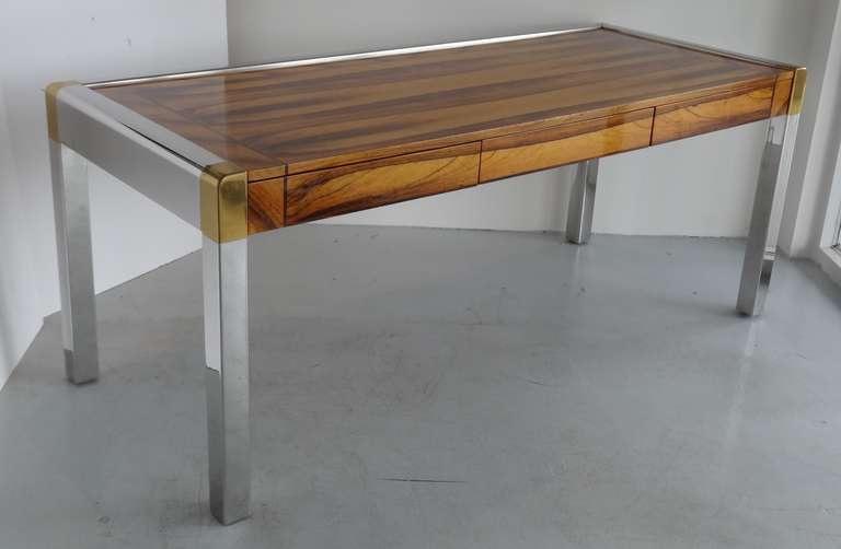 Stunning to say the least. A large custom desk by Karl Springer. Stainless steel brass and natural rosewood. 3 deep drawers with one having a removable pencil canoe. Note the exquisite work on the wood, as well as the seamless metal joints.