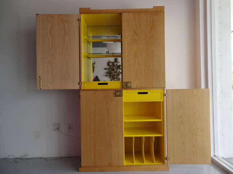 A handsome Mid-Century bar cabinet by Tommi Parzinger, the exterior is cerused oak with iconic brass hardware. The interior done in bright yellow has multiple compartments and drawers. The top is lighted and the back is mirror. A couple of the