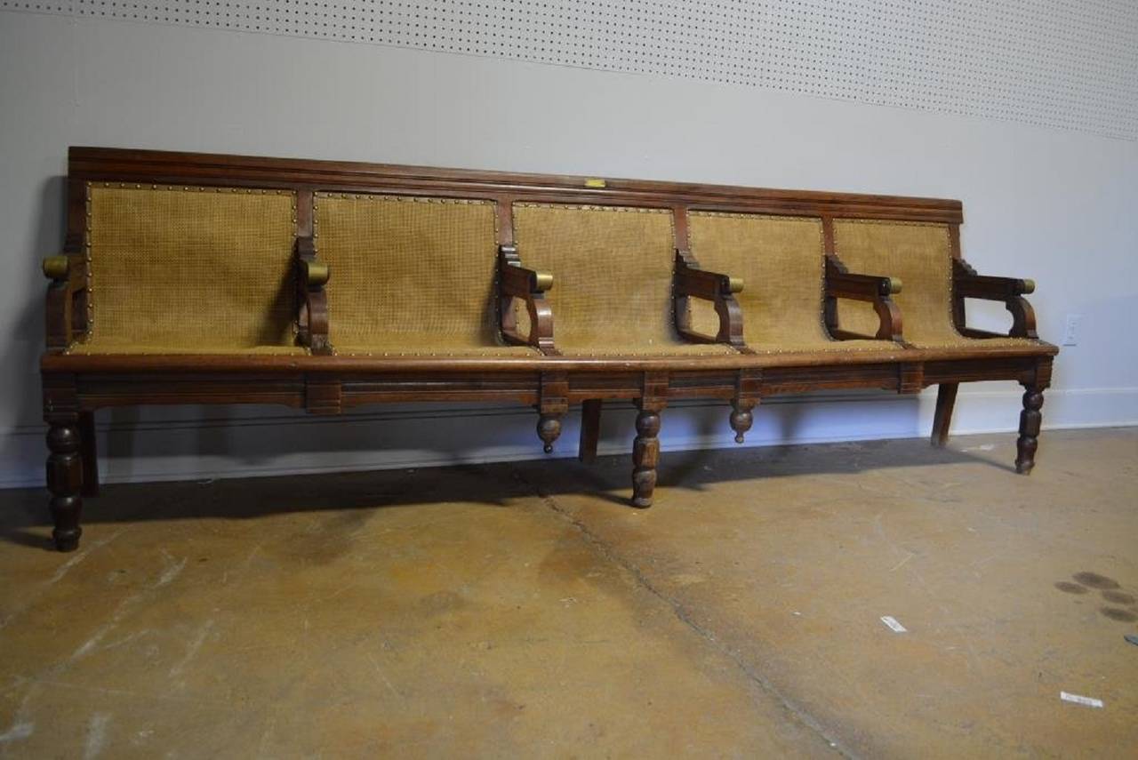 Antique American railroad station wood bench with brass arms and linen upholstery.