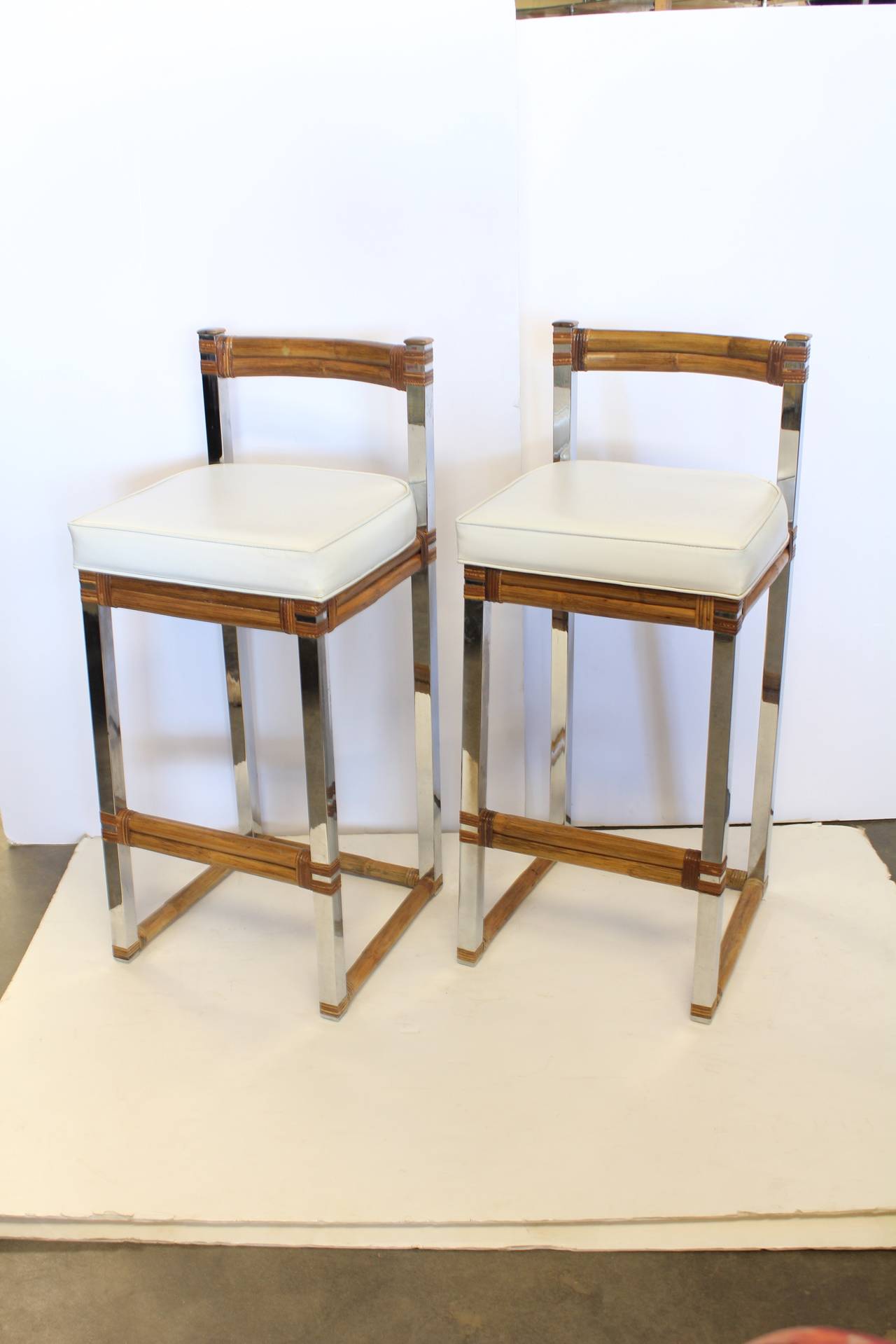 Stylish set of Mid-Century chrome and rattan bar stools with original white vinyl upholstery.