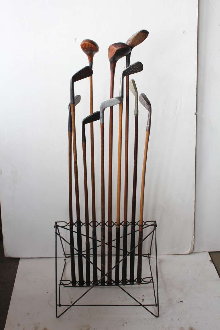 Antique iron folding stand with antique golf clubs.