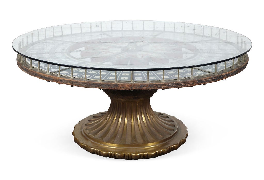 Oversized roulette wheel game table with glass top and bronze base.