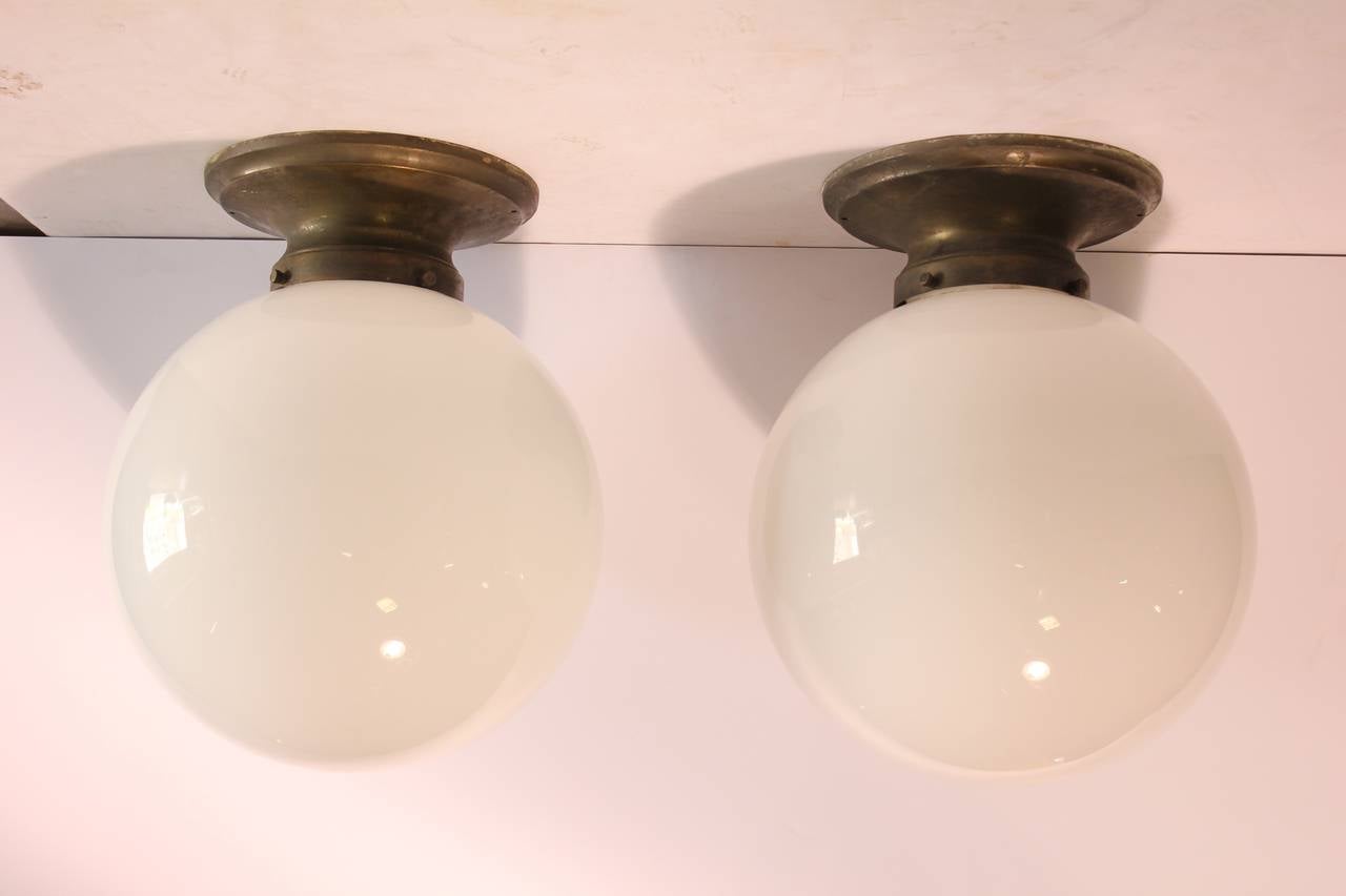 Large antique Industrial school lights with large white glass globes and brass holders.