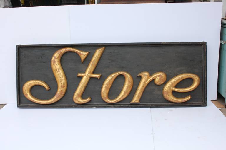 Antique department store sign made of gilded cast iron letters attached to black board.