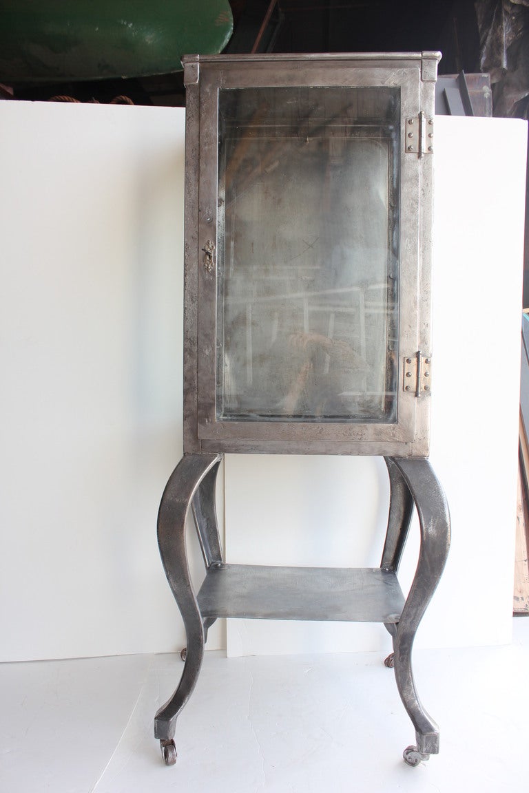 Antique steel medical display cabinet with glass sides and cast iron legs. It has two shelves.