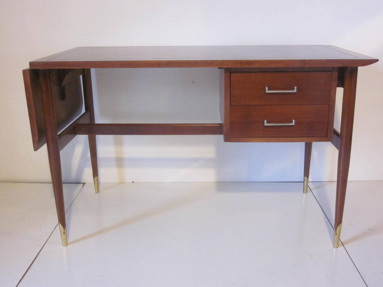 A dark walnut Altavista desk with drop leave extension to one side, two floating drawers under the top with metal pulls and brass end caps to the conical legs. With the drop leave up the total length is 60