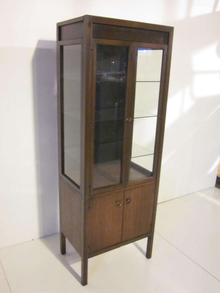 A walnut and rose wood detailed light up display cabinet with two doors,three adjustable glass shelves,three sides of display glass and lower doors with drawers. Bronze pulls complement the doors and cabinet, a hard to find Mid Century design.