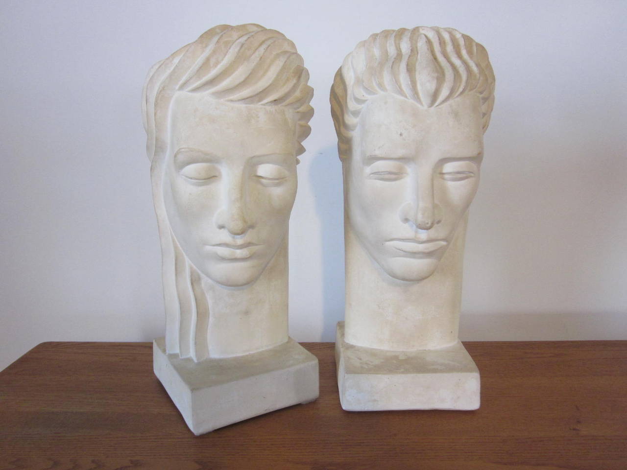 A pair of Art Deco styled busts of a streamline designed male and female cast in plaster with great age and patina.