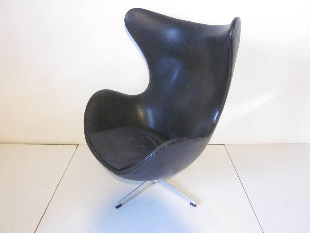 A black leather Jacobsen swiveling egg chair with aluminum base with rubber foot pads, retains the factory labels manufactured by Fritz Hansen made in Denmark.