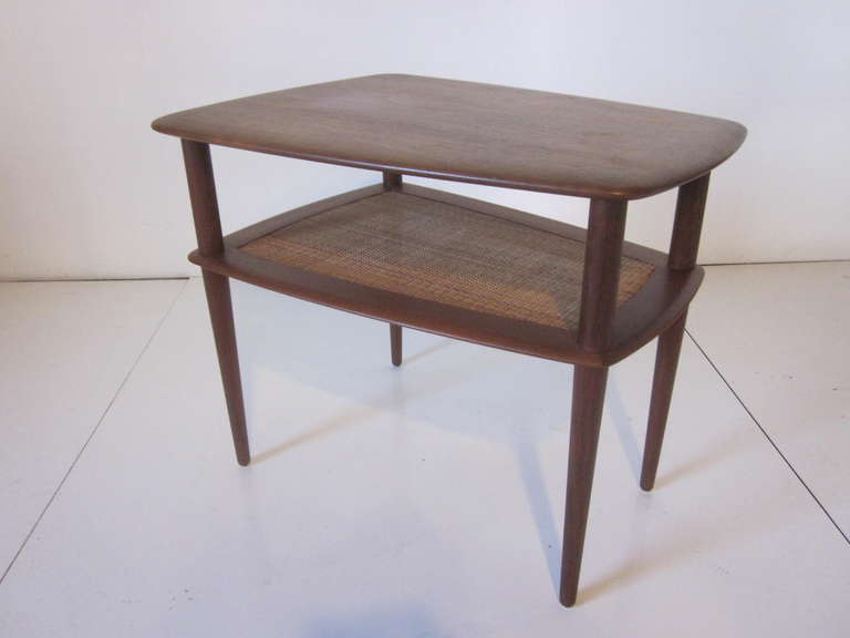 A simple but refined Hvidt side table with caned second shelve and concial legs in a medium dark teak wood,retains the manufactures tags and imprint made in Denmark.