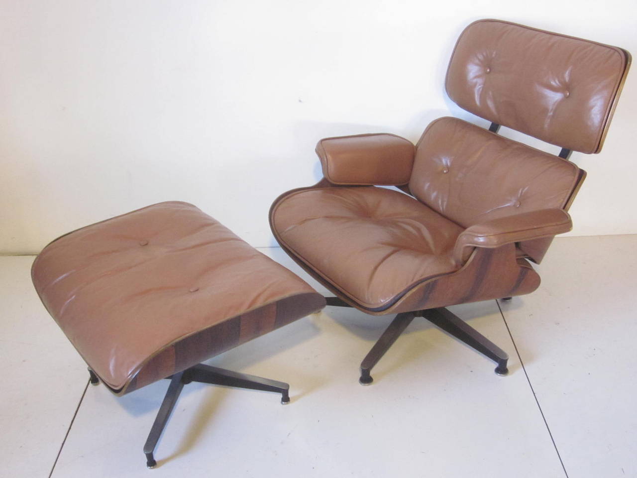 A beautifully grained rich Brazilian rosewood Eames lounge chair with matching ottoman and custom ordered saddle tan colored leather cushions. This swiveling chair with ottoman sits on cast aluminum bases. Retains the original manufactures labels
