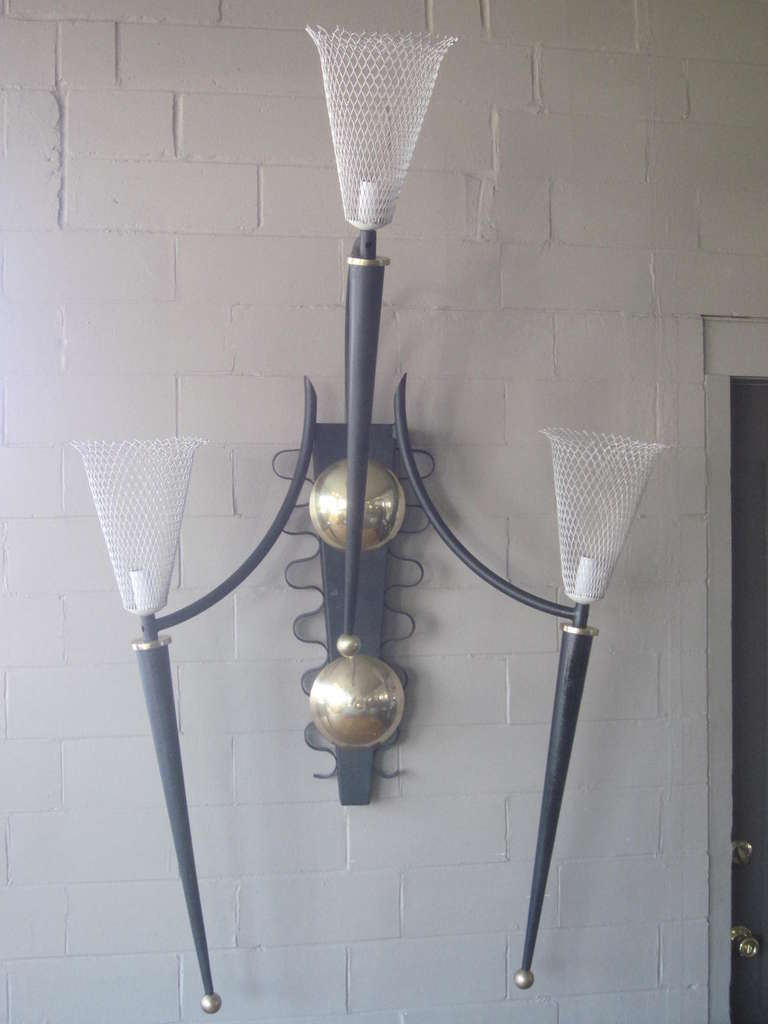 A large monumental theater sconce with wire basket shades in the style of Mathieu Mategot France , black metal horns and brass roundels, balls and details. A very well made and impressive piece of sculpture designed by P.Marchand and made in the