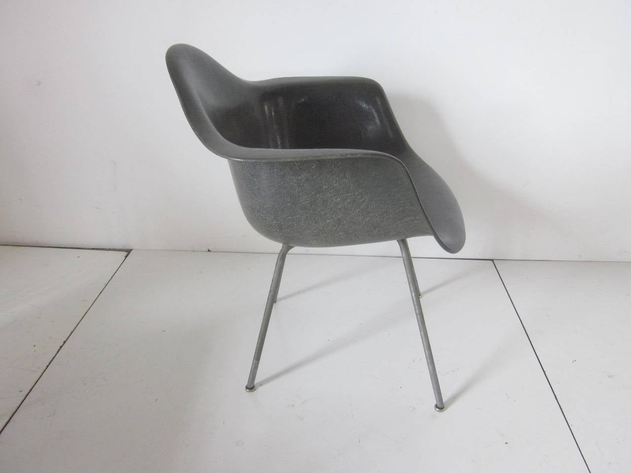 A very early Eames fiberglass arm shell chair in elephant gray, rope edge, zinc X-base legs and large early rubber shock mounts. Retains the manufactures decal to the front bottom Zenith company Herman Miller, Charles Eames design.