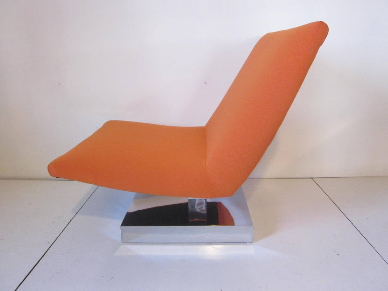A tangerine colored upholstered lounge chair sitting on a chrome platform base in the manner of Milo Baughman.