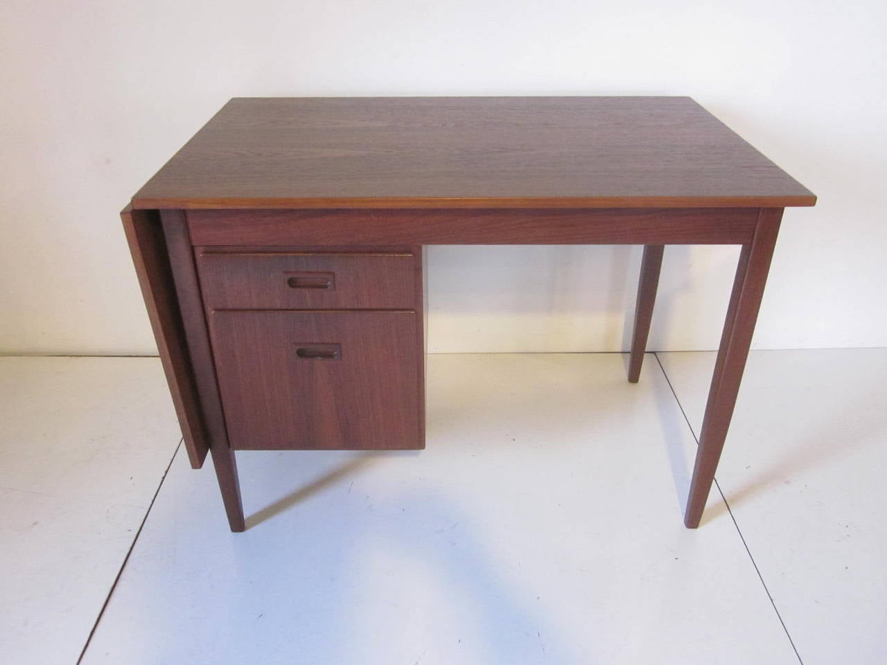A teak desk with sliding top which can be extended or folded down depending on your requirements, also the bank of two drawers can be slid for right or left hand use. With top extended it is 60