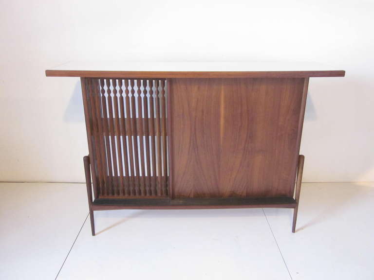 A nice sized Mid Century dry bar with architectural inspired sculptural design and wonderfully grained walnut front , foot rest, white Formica top and reverse side shelves for bottles and glass wear even a old fashion bottle opener.