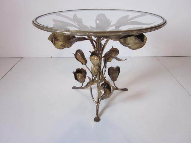 A gold/bronze toned gilt metal occassional table with a sculptural floral design and inset glass top.